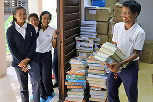 JPA Image Gallery - A high school student smiles as he walks out of the storeroom with his pile of books - Jay Pritzker Academy, Siem Reap, Cambodia