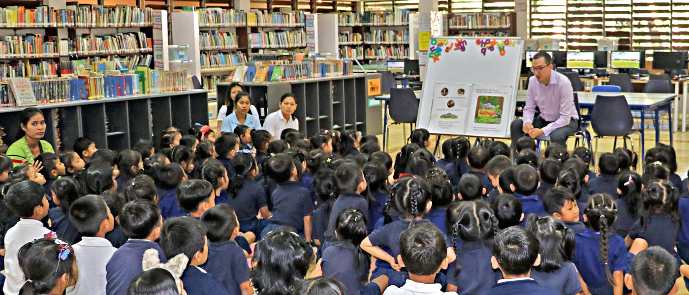 JPA students celebrating book week 2018 listening to a story in the library. Jay Pritzker Academy, Siem Reap, Cambodia. Jay-Pritzker-Academy-Siem-Reap-Cambodia.